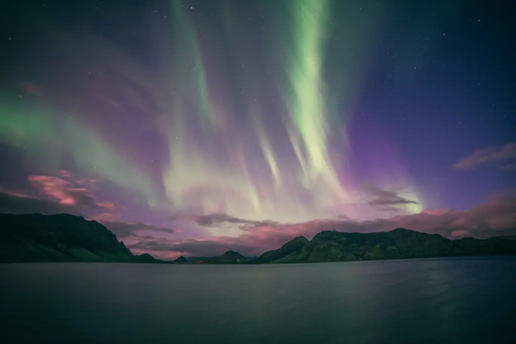 Green and purple northern lights over a dark lake and mountains in Iceland