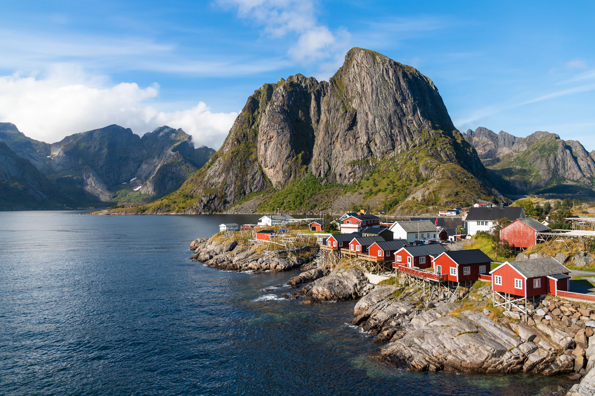 Red fishing cabins on the shore beneath steep peaks in Lofoten